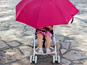 Little girl with a pink umbrella in an umbrella stroller